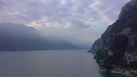 Dolly-out-drone-shot-revealing-the-tall-mountains-right-next-to-Riva-del-Garda,-Lombardy