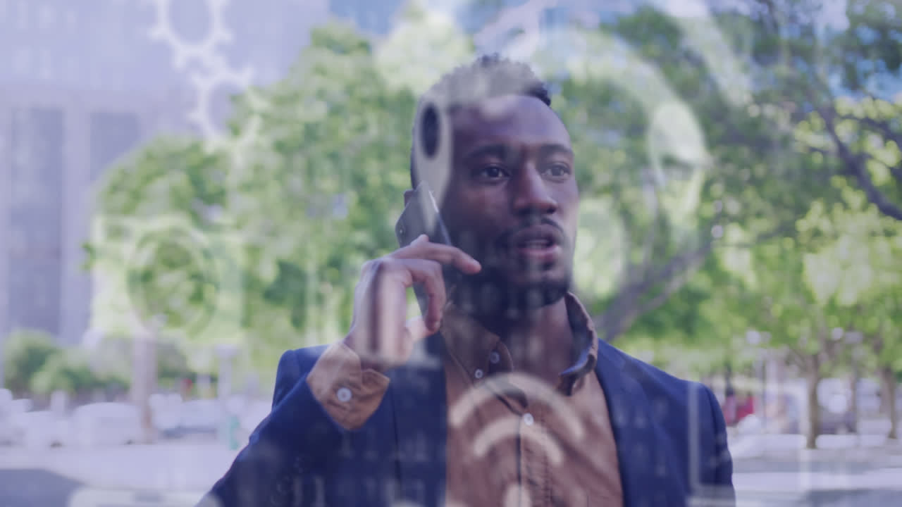 varios iconos digitales flotando contra un hombre afroamericano hablando en su teléfono inteligente en la calle