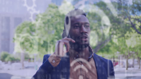 multiple digital icons floating against african american man talking on smartphone on the street