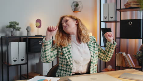 happy businesswoman at home office desk closing laptop and stretching arms after finishing work