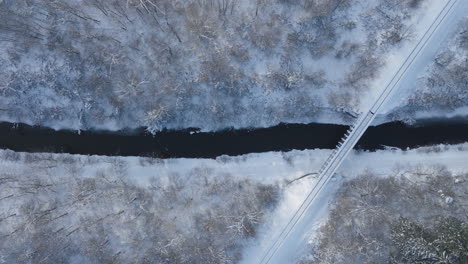 winter bridge crossing over partially frozen river, aerial top down