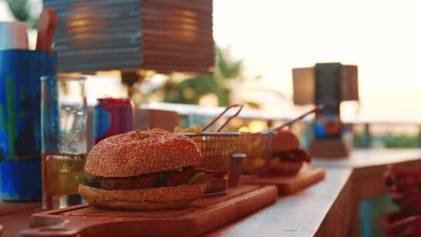 persona comiendo hamburguesas y papas fritas en un restaurante al aire libre durante la puesta de sol en el caribe