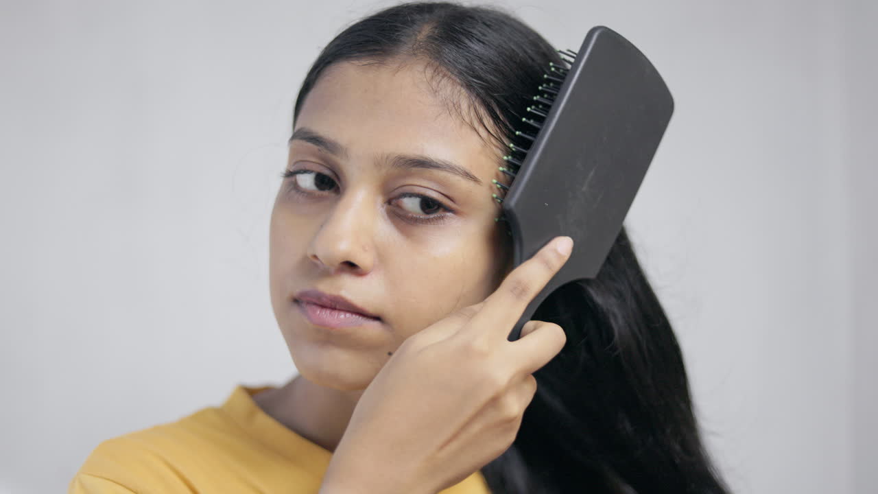 Indian young woman combing her hair with hair brush in white background, hair care concept.