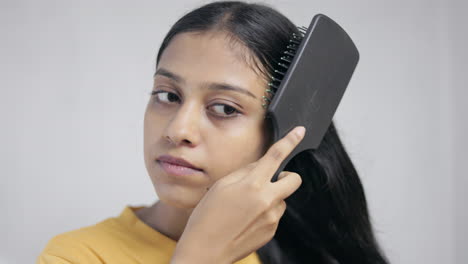 indian young woman combing her hair with hair brush in white background, hair care concept.