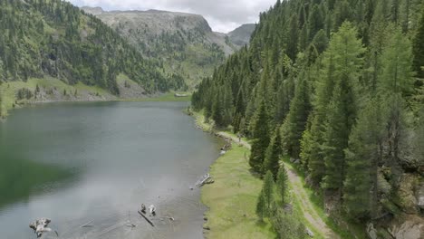 Antenne-Rückwärts-Steigender-Schuss-Zeigt-Mountainbiker,-Die-In-Den-Bergen-Entlang-Des-Seewegs-Fahren