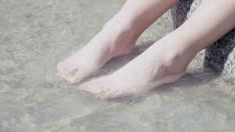 이탈리아 알프스의 계곡 한가운데 있는 바위에 앉아 다리와 발을 물에 담그고 있는 어린 소녀들
