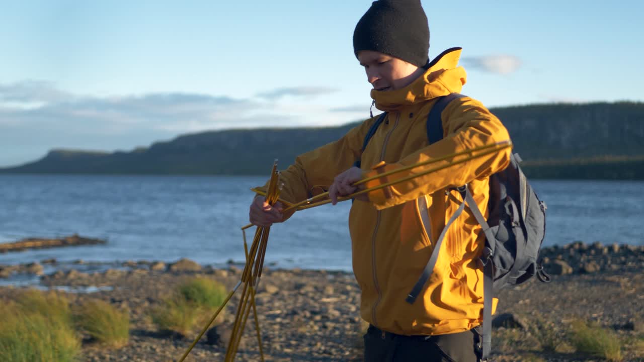 Connecting Tent poles together to raise camping tent near Swedish lake - Medium push in tracking slow motion shot