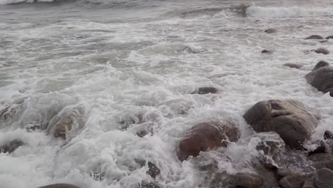 Foamy waves crashing over rocks panning right