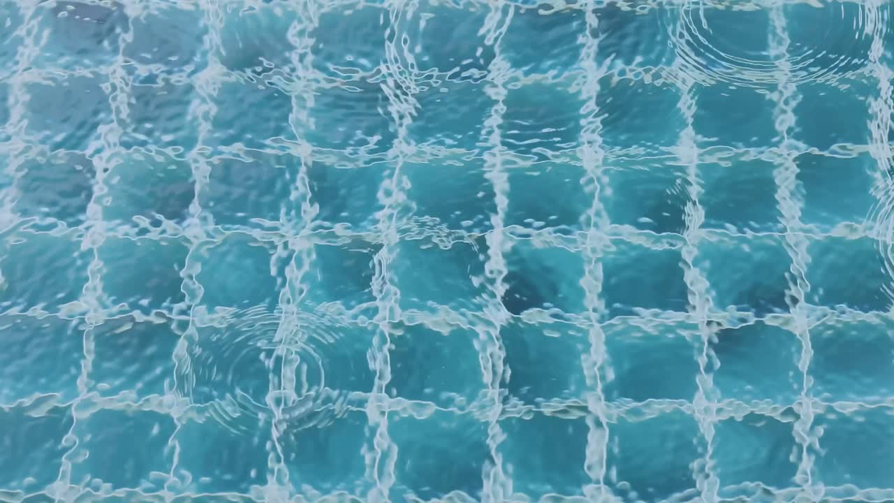 Pemandangan tenang tetesan hujan menciptakan riak-riak di permukaan kolam berubin, tertangkap dalam pencahayaan lembut.