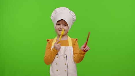 Child-girl-kid-dressed-cook-chef-baker-in-apron-and-hat-with-plastic-fork-and-knife-fooling-around