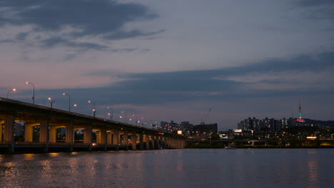 Illuminated-Banpo-Bridge-at-Sunset,-View-of-N-Seoul-Tower-and-Colorful-Lights-Reflections-in-Calm-Han-River-Water---copy-space-realtime