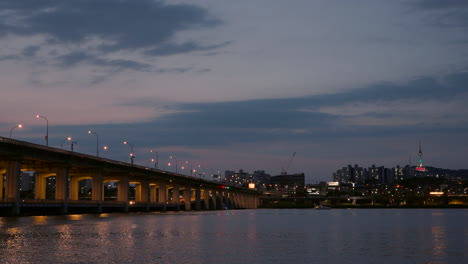 illuminated banpo bridge at sunset, view of n seoul tower and colorful lights reflections in calm han river water - copy space realtime