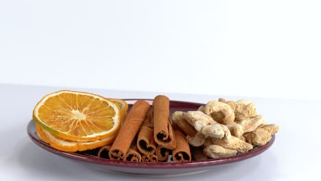 Dried-orange,-Cinnamon-sticks,-and-Ginger-root-on-plate-against-white-background