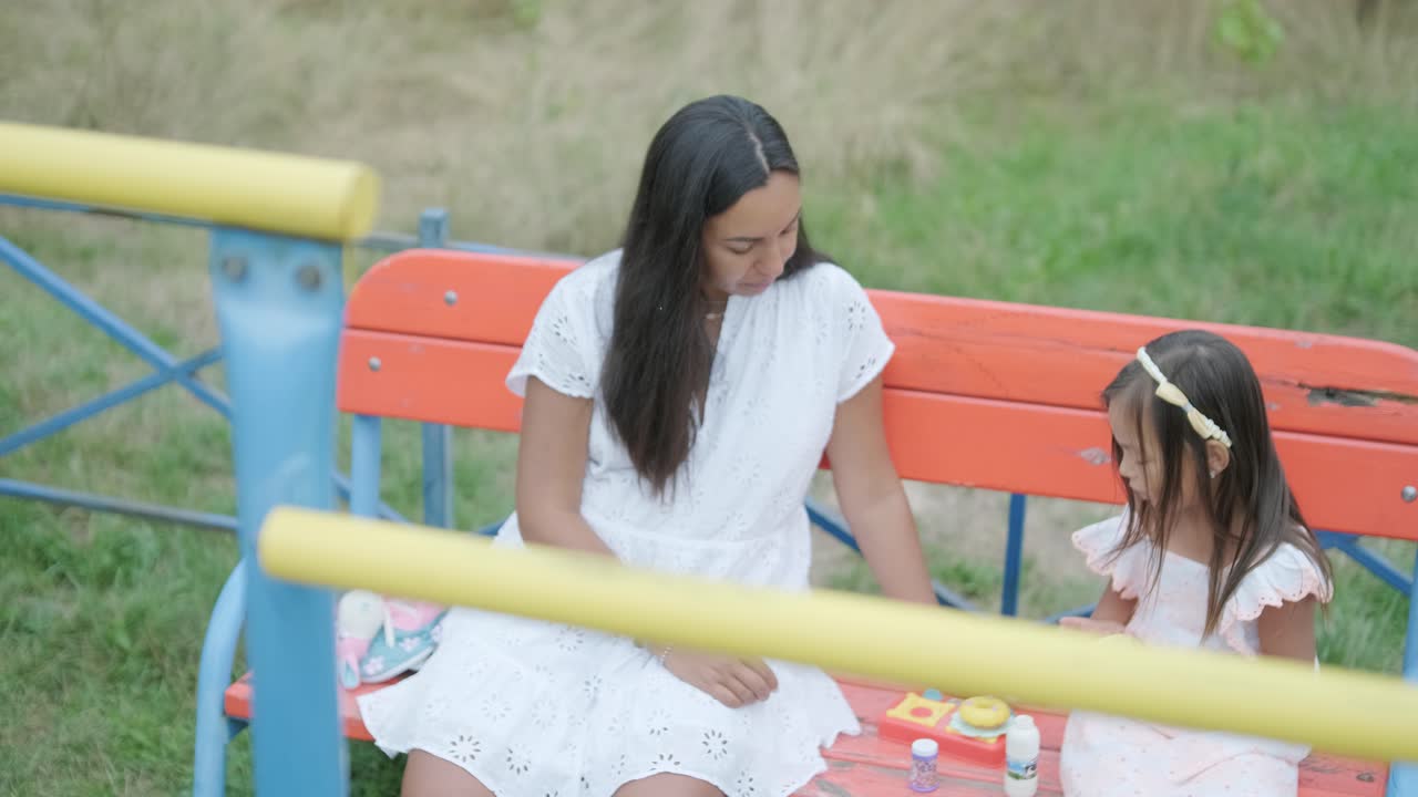 임신 한 어머니 와 어린 딸 은 나무 와 초록색 으로 둘러싸인 공원 의 놀이터 에서 함께 놀이 를 즐긴다