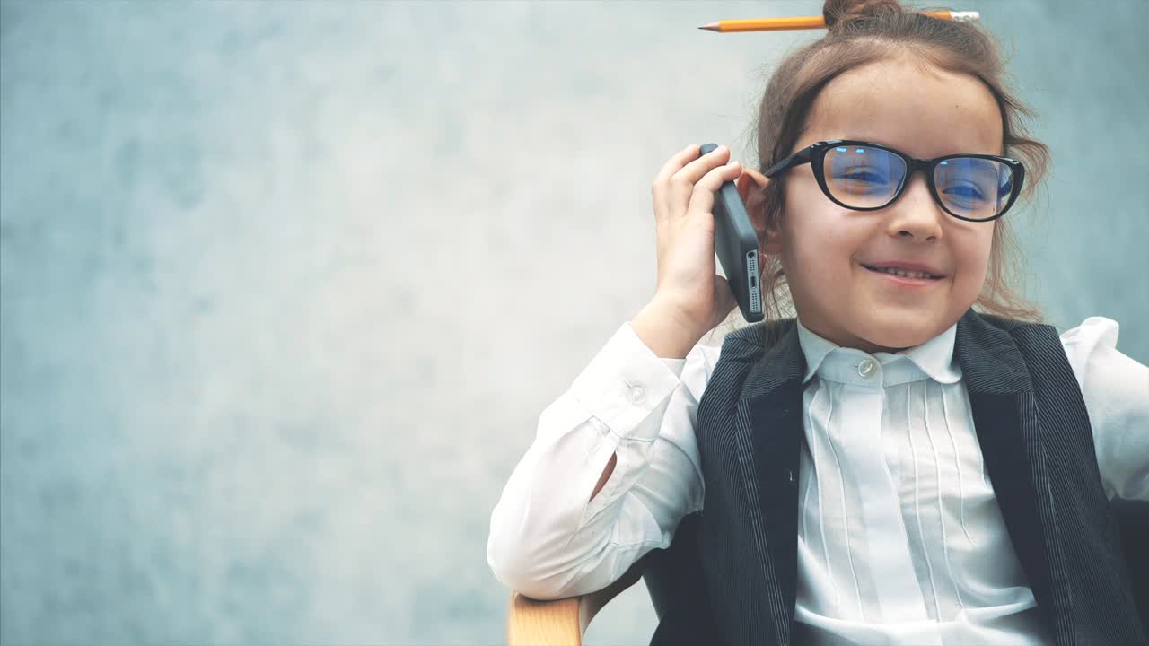 Close-up of a small business girl sitting on a chair on a gray background. During this, he speaks by phone and smiles.