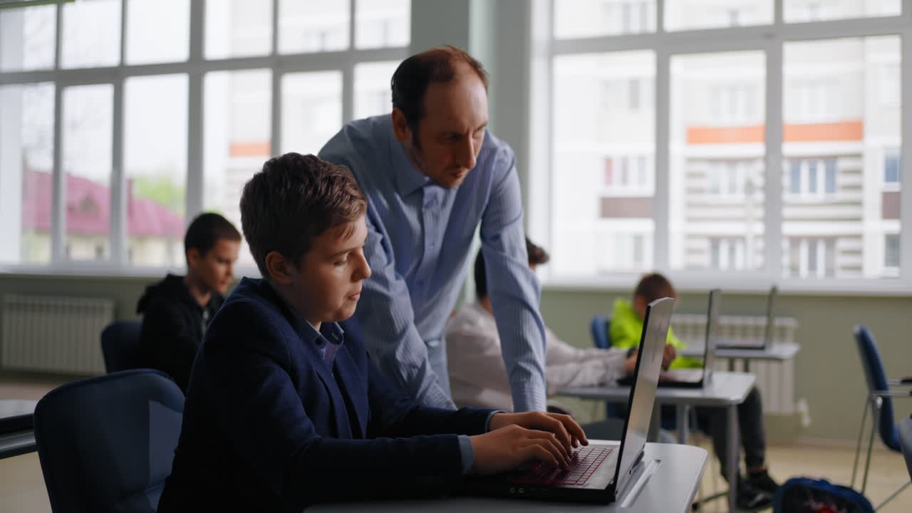Teacher assisting student with laptop in classroom