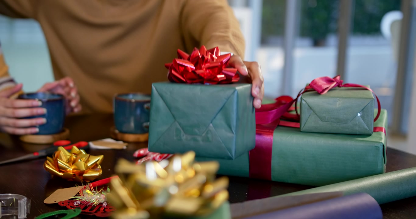 Coppia afroamericana a tavola, con l'uomo in maglione marrone che allunga la mano verso un fiocco rosso, offrendo un regalo di Natale.