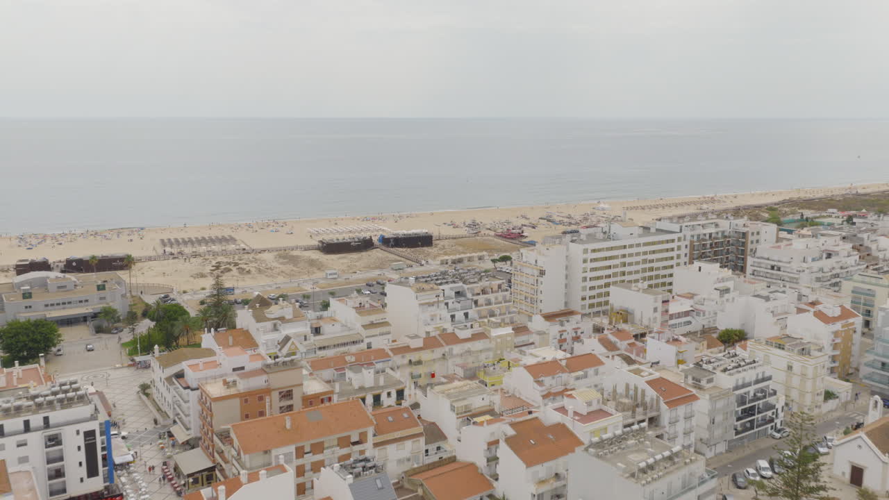 Drone vola in avanti sopra i tetti di Monte Gordo verso spiagge, ombrelloni e mare
