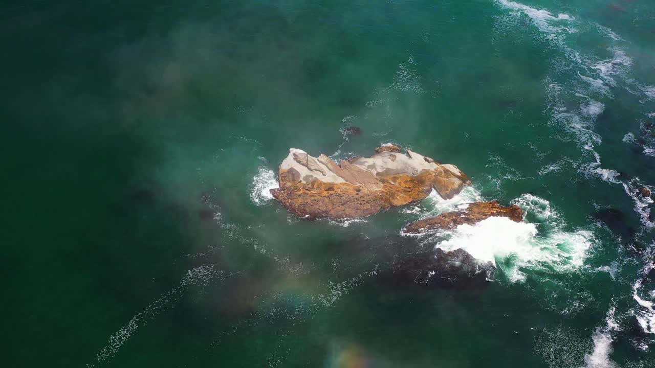Scenic static aerial shot of a rocky formation in the ocean with waves and low flying clouds by the coastal shore of Oregon, Pacific Northwest.
