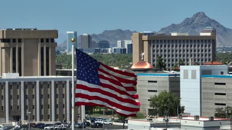 american flag with phoenix, arizona state capitol and government buildings in background