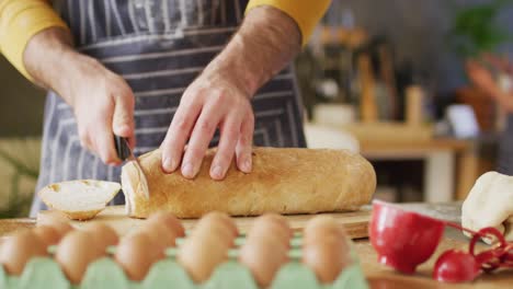 video of midsection of caucasian man in apron slicing bread in kitchen, with copy space