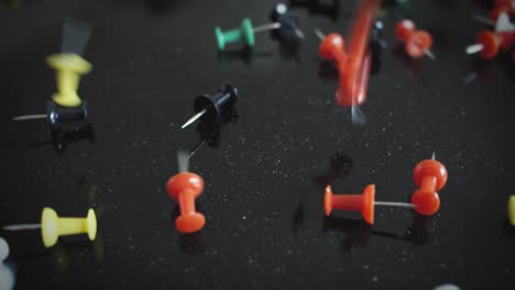 cientos de tachuelas de colores caen sobre una superficie negra reflectante