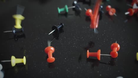 hundreds of colorful pinboard tacks fall onto a reflective black surface