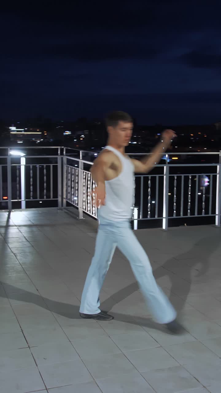 Male dancer performing dynamic movements on rooftop at night with city lights in the background