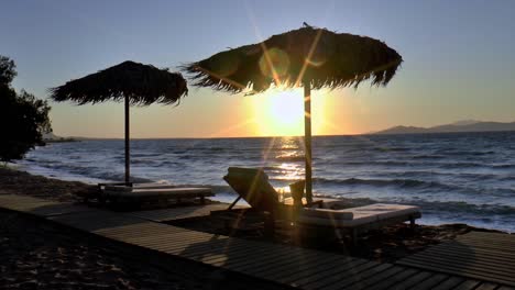 Sonnenschirme-Aus-Palmblättern-Und-Sonnenliegen-Im-Sonnenuntergang-Am-Strand-Von-Kos