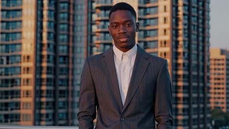 confident young black businessman wearing tailored suit standing on urban rooftop with expansive city skyline, embodying professional success and entrepreneurial spirit during golden hour lighting