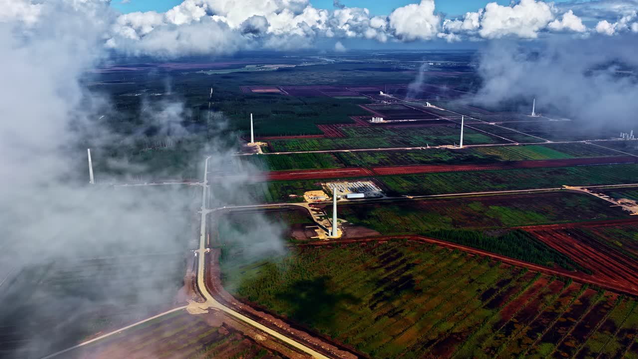 Aerial shot of wind turbines through drifting low cloud over a patchwork of red soil agricultural fields and green crops