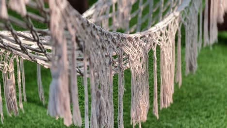 An-empty-hammock-with-dangling-rope-decorations-is-installed-on-the-grass