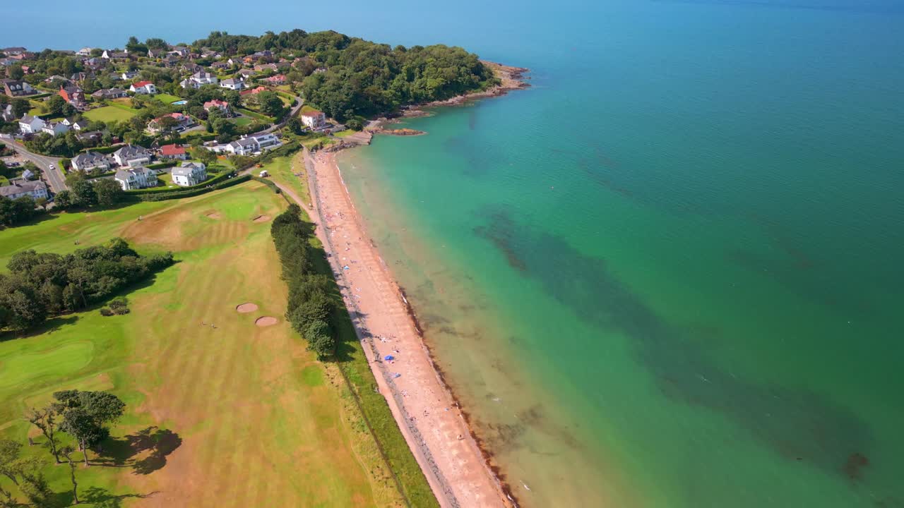 Centreret baglæns luftvideo af Helen's Bay strand i County Down, Nordirland, Storbritannien på en lys sommerdag. Filmet i 4K, 60FPS og med Rec709 farve.