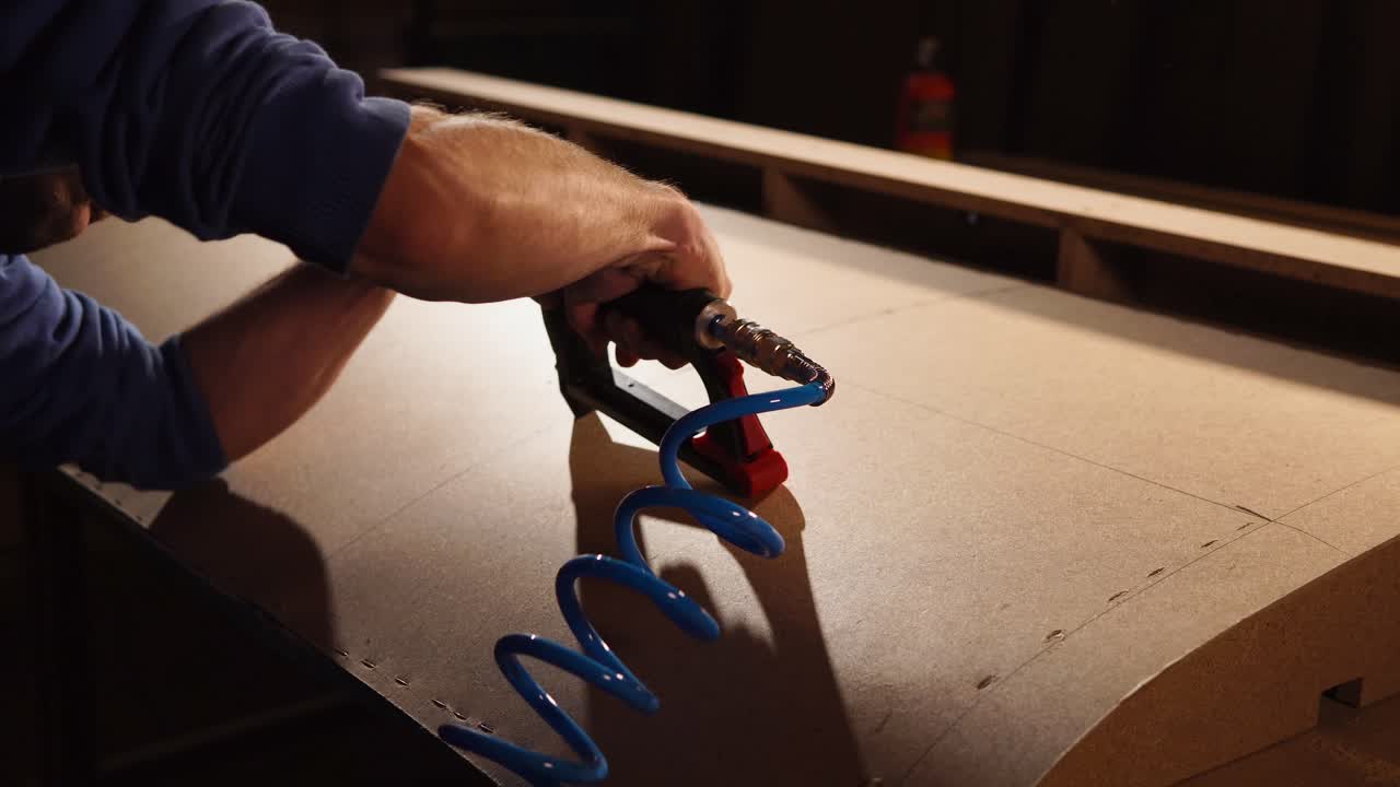 hombre usando una pistola de clavos para montar un panel de madera curva