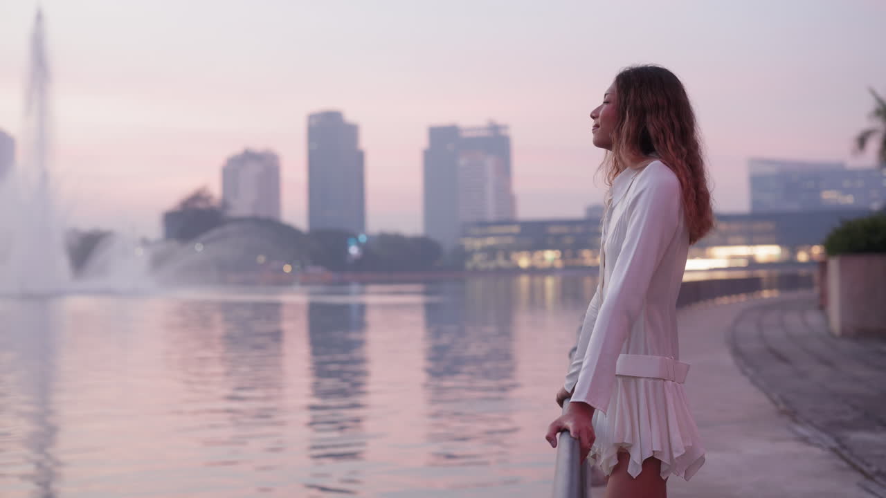 Elegant Woman Enjoying Sunset by City Lake with Fountains and Skyline