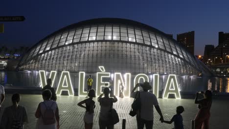 Turistas-Tomando-Fotografías-Nocturnas-Frente-A-Letras-En-Valencia,-Hemisférico-En-La-Ciudad-De-Las-Artes-Y-Las-Ciencias,-España