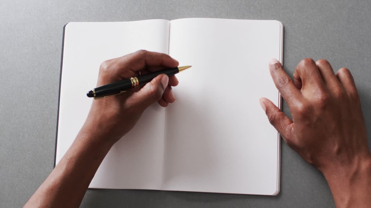 Close up of hand writing with pen on book with copy space on gray background in slow motion