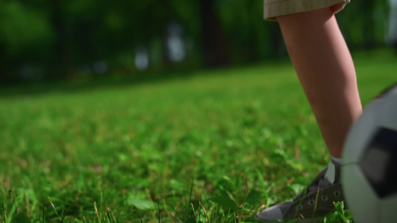 모르는 아이들의 발이 잔디 위에서 축구를 하고 있다. 소년의 다리가 공원에서 공을  ⁇ 는다.