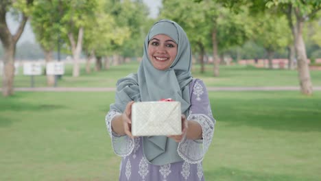 happy muslim woman giving a gift in park