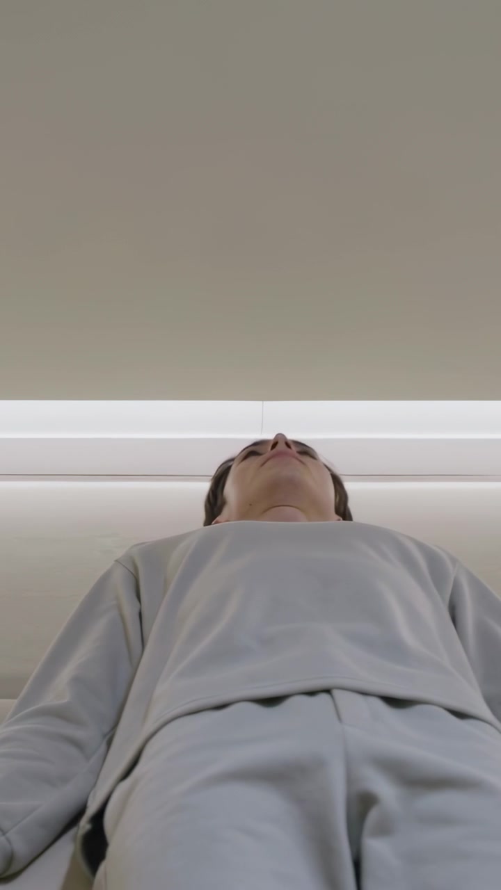 Vertical video: Rising man lifting torso from recline to gaze under LED trim at home in grey-sweats