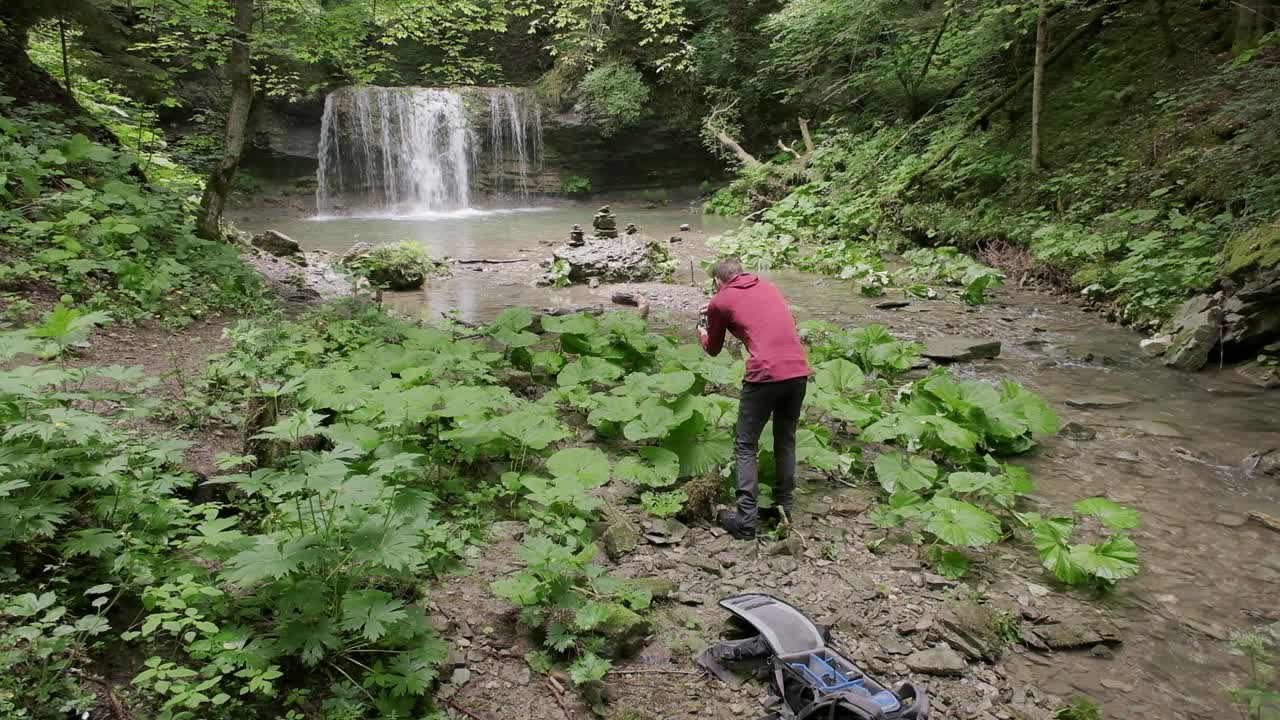 toma de gran angular con un fotógrafo caminando a través de las plantas bajas encontrando una composición con una cascada en el fondo