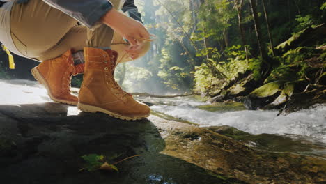 female hands lace up the female on a trekking boot in the forest in the background a mountain river