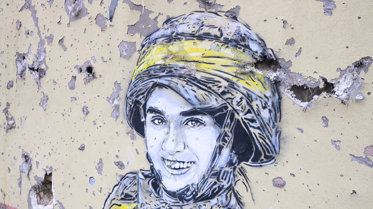 A close-up of a mural depicting a Ukrainian soldier, surrounded by real bullet and shrapnel holes, on a war-damaged building in Irpin, Ukraine, during the Ukraine-Russia conflict.