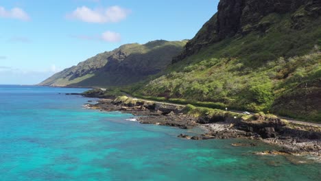 aerial view of a coastal road winding beneath lush volcanic cliffs near makapuʻu point, oahu. turquoise waters crash against rugged shoreline, showcasing hawaii’s dramatic island scenery