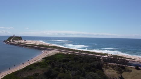 Drone-Ascendiendo-Sobre-Una-Península-Con-Un-Faro-Y-Playas-De-Arena