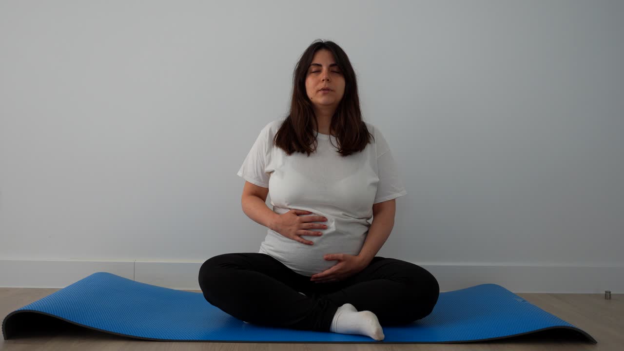 Pregnant woman doing breathing exercises on a blue mat at home