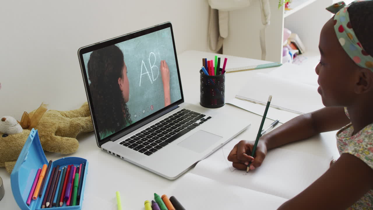 African american girl doing homework while having a video call with female teacher on laptop at home