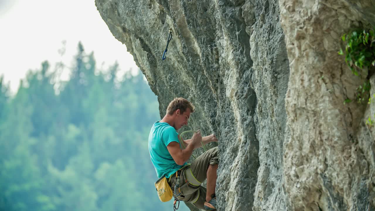 young fit rock climber fastening safety rope to carabiner. Vertical rock wall