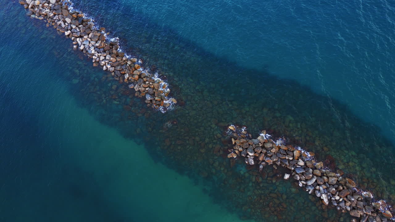 Clear aerial view of rocks lining the Mediterranean coast, waves gently lapping at the shore
