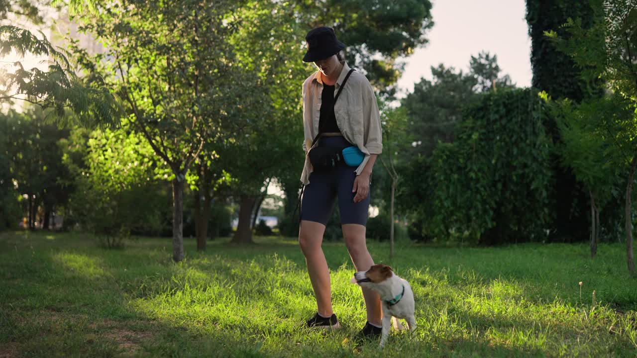 한 여자가 공원에서 개를 산책시키고 있다.